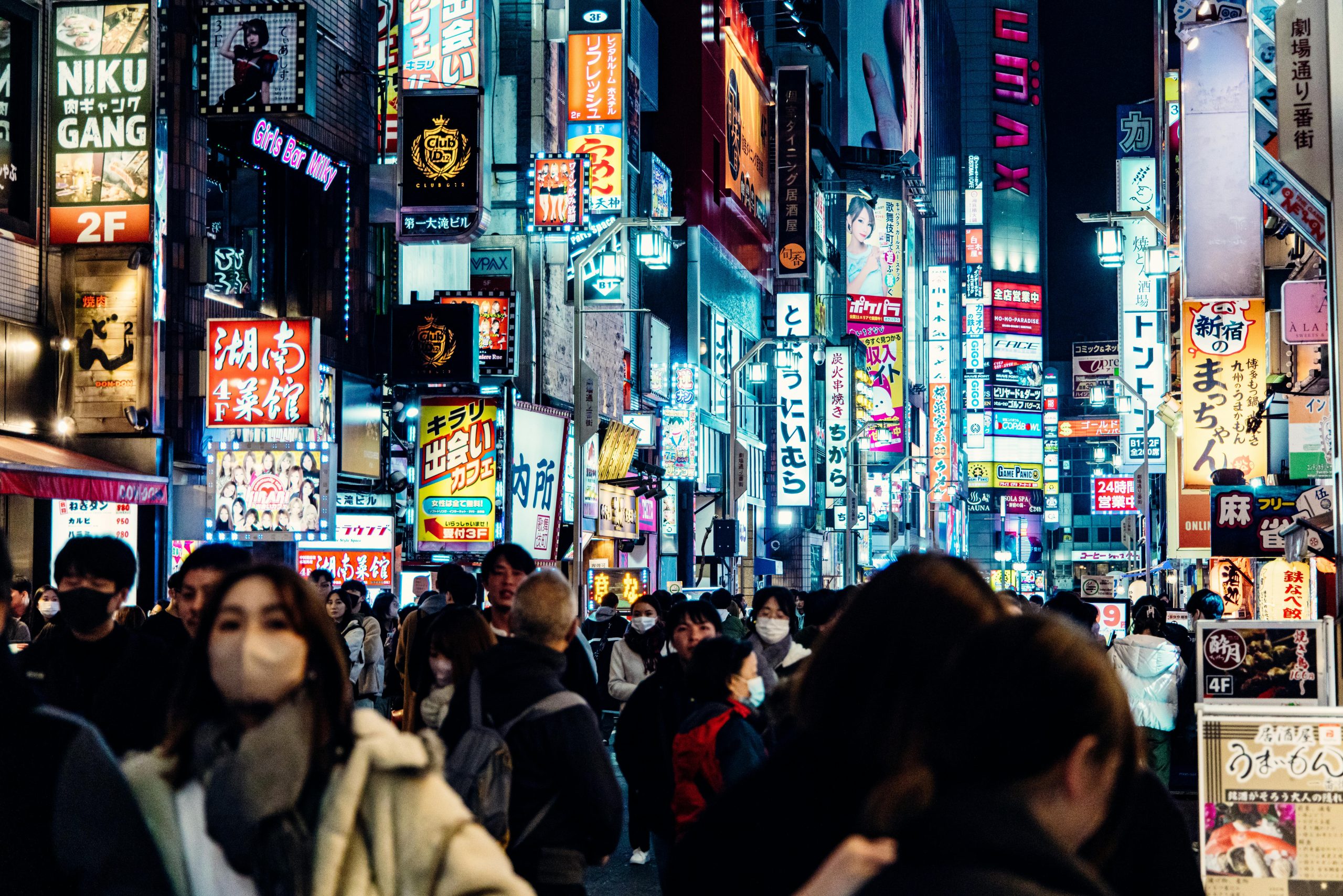 Crowds navigate the vibrant neon-lit streets of Shinjuku, Tokyo's nightlife epicenter, filled with signs and energy.